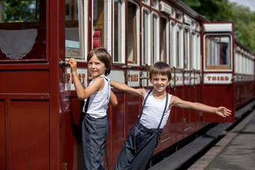 Wall Mural - Beautiful children, dressed in vintage clothes, enjoying old steam train on a hot summer day