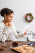 © LIGHTFIELD STUDIOS - Young african american woman using digital tablet near blurred gingerbreads and flour in kitchen