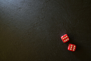 The two red dice with the highest score lie on a black stone surface. The light falls from the left. Background. Texture.