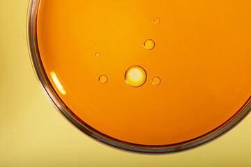 Top view of petri dish with cosmetic oil inside.Yellow background with copy space,macro photography.