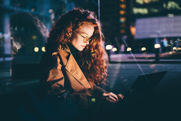 Woman using laptop on night city street.