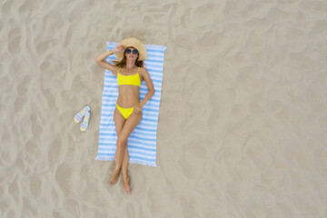 Canvas Print - Woman sunbathing on beach towel at sandy coast, aerial view. Space for text