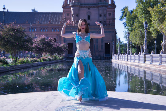 Middle-aged Hispanic woman in turquoise dress with rhinestones, raising her dress while belly dancing. Belly dance concept.