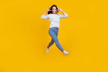 Wall Mural - Full length photo of happy positive young woman jump up walk make v-signs cool isolated on yellow color background