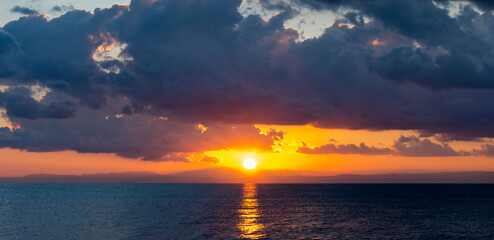 Wall Mural - Stunning dramatic, cloudy sunrise with a bright sun rising over a calm water. Natural background, Sardinia, Italy.