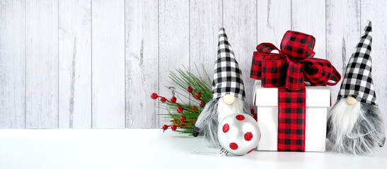 Web banner. Christmas farmhouse theme background backdrop styled with gift with buffalo plaid bow and farmhouse style gnomes against a white wood background. Negative copy space.