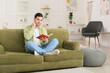 © Pixel-Shot - Young man reading book and listening to music at home