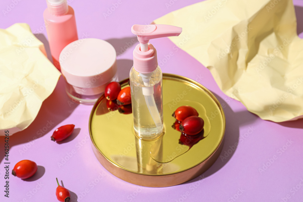 Different cosmetic products and rose hip berries on lilac background