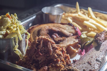 american barbecue tray with porchetta, pulled pork, coleslaw salad, brisket, barbecue sauce, pulled pork dumpling, french fries, selective focus