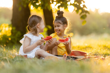 Two kids eating of watermelon in the garden. Kids eat fruit outdoors. Healthy snack for children. Girls enjoying watermelon. The concept of a healthy lifestyle. Happy childhood. Space for text.