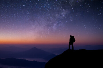 Wall Mural - A young tourist with a bag is standing looking at the stars. The Milky Way and the beauty of the night sky alone on the top of the mountain. He felt successful at reaching his intended destination.