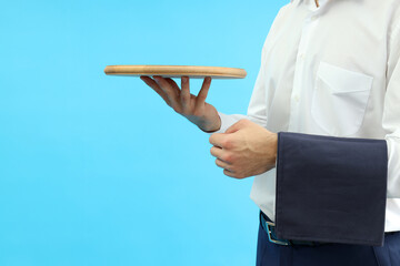 Wall Mural - Young man waiter holds tray on blue background, space for text