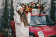 © polinaloves - Happy beautiful woman wearing knitted sweater and woolen hat standing near red car with Christmas tree on the top under snowfall.