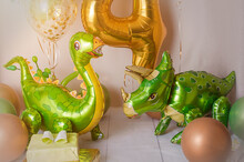 Room Decorated For A Birthday Party With Golden, Green And Yellow Baloons, Large Inflatable Number 4, Dinosaur Baloons.