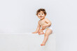 Portrait of cute smiling toddler boy, baby in diaper sitting isolated over white studio background. Happy child
