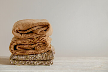 Bunch of knitted warm pastel color sweaters with different knitting patterns folded in stack, clearly visible texture. Stylish fall-winter season knitwear clothing. Close up, copy space for text.