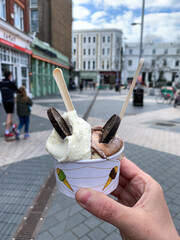 Woman’s hand is holding cup with two ice cream scoops. Vanilla and hazelnut ice cream with chocolate 