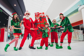 Poster - Portrait of attractive cheerful funky company elfs demonstrating giftboxes festal eve tradition christmastime at mall indoors