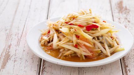 Som Tum Pla Ra, Thai E-San food, spicy papaya salad with pickled fish, tomato, lime and chilli in white ceramic plate on white wood texture background with copy space for text