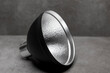 Small black speedlite flash light modifier reflector for illumination against a modern contemporary gray background with silver inside. Photography accessory studio still life.