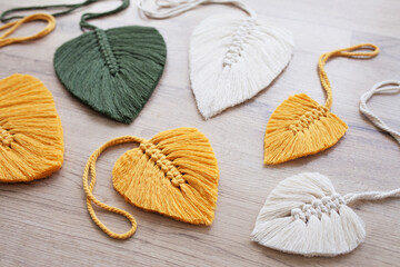 Macrame leaves in yellow, green  and natural color on the wooden background. Cotton rope decor macrame to make your home more cozy and unique.