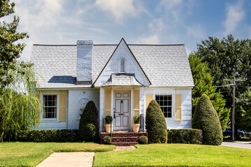 Cute yellow and white brick and siding cottage with pretty lawn and landscaping and shutters in leafy neighborhood.