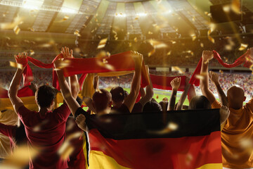 Wall Mural - Back view of football, soccer fans from Germany cheering their team with black red yellow flags and scarfs at stadium.