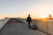 © VITTA GALLERY/Westend61 - Spain, Barcelona, back view of  young businessman with rolling suitcase at sunset