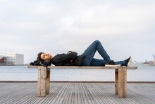 Denmark, Copenhagen, Young Man Lying On A Bench At The Waterfront