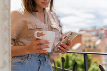 Close-up Of Woman On Balcony In The City With Coffee Cup And Cell Phone