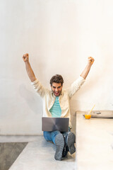 Cheering man sitting on a step using laptop
