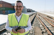 © Hernandez and Sorokina/Westend61 - Portrait of smiling man on railway tracks in front of cargo containers with cell phone