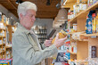 © Westend61 - Senior man with smartphone buying groceries in a small food store