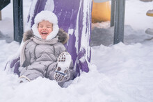Laughing Child On A Slide In Winter Day. Happy Childhood. Outdoor Games In Winter