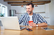 © Bartek Szewczyk/Westend61 - Smiling man working remotely on laptop at home and having coffee