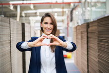 Portrait Of Happy Businesswoman In Factory Warehouse Shaping A Heart With Her Hands