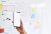 Male Hand Holding Aloft A Smartphone In Front Of A Whiteboard