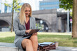 © Daniel Ingold/Westend61 - Smiling blond businesswoman sitting on a wall outdoors using digital tablet