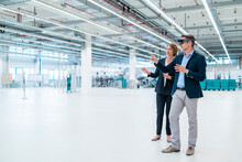Businessman With AR Glasses And Businesswoman In A Factory Hall