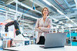 © Daniel Ingold/Westend61 - Smiling businesswoman with laptop in a modern factory hall