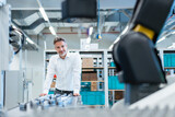 Fototapeta Las - Confident businessman in a modern factory hall looking at robot
