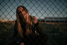 Portrait Of Young Woman Sitting Behind Wire Mesh Fence Giving The Finger