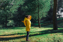 Girl Wearing Yellow Raincoat And Yellow Backpack Standing On A Meadow At Sunlight