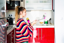 Girl Playing With Microphone And Smartphone In Kitchen At Home