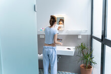 Rear View Of Young Woman Brushing Teeth In Bath Room