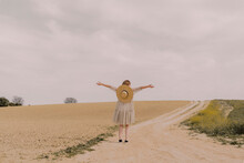Woman With Straw Hat And Vintage Dress Alone At A Remote Field Road In The Countryside