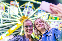 Portrait Of Mother And Daughter Taking Selfie In Front Of Big Wheel At Fair