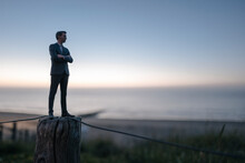 Businessman Figurine Standing On A Fence At The Beach, Looking At The Sea
