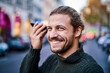 © Jo Kirchherr/Westend61 - Portrait of laughing young man using smartphone on the street in the evening