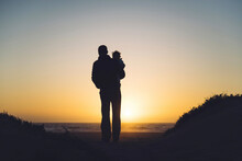 USA, California, Morro Bay, Silhouettes Of Father And Baby Enjoying Sunset On The Beach
